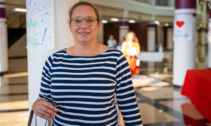 A woman wearing a striped shirt smiles while standing in a school hallway